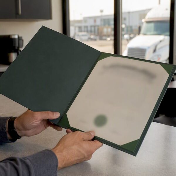 1787384218004_Hands-holding-certificate-holder-folder-at-trucking-office Hands holding certificate holder folder at trucking office